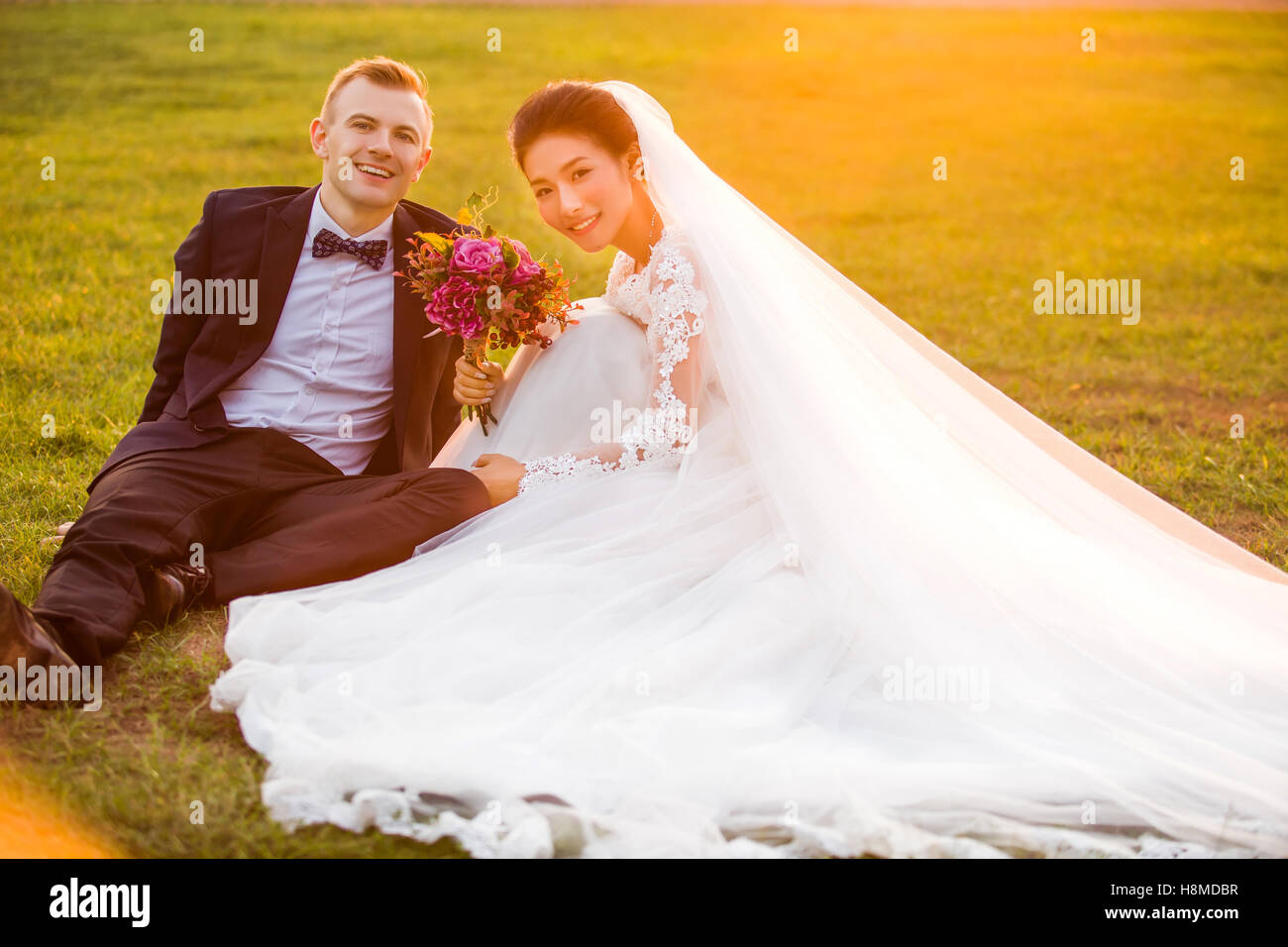Portrait of smiling wedding couple sitting on grassy field Stock Photo ...