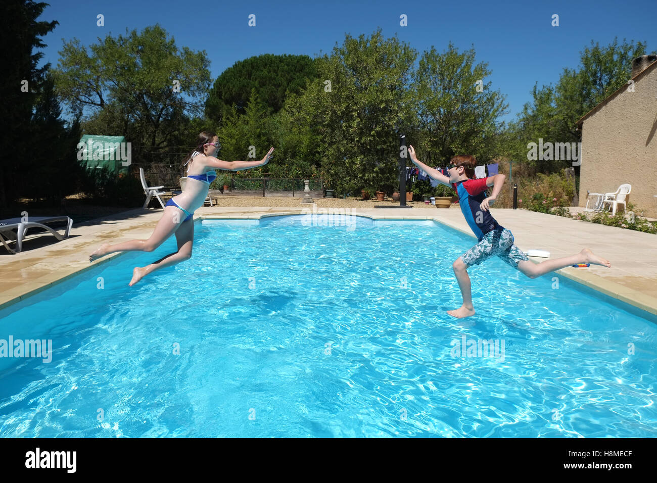 two children jump towards each other trying to touch hands in a swimming pool laughing and having fun Stock Photo