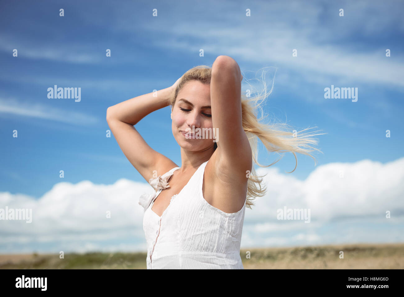 Blonde woman standing in field with hand in hair Stock Photo