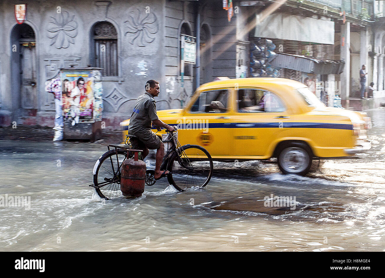 During the Indian monsoon a man cycles through floodwaters in historical Kalighat, Kolkata, India Stock Photo