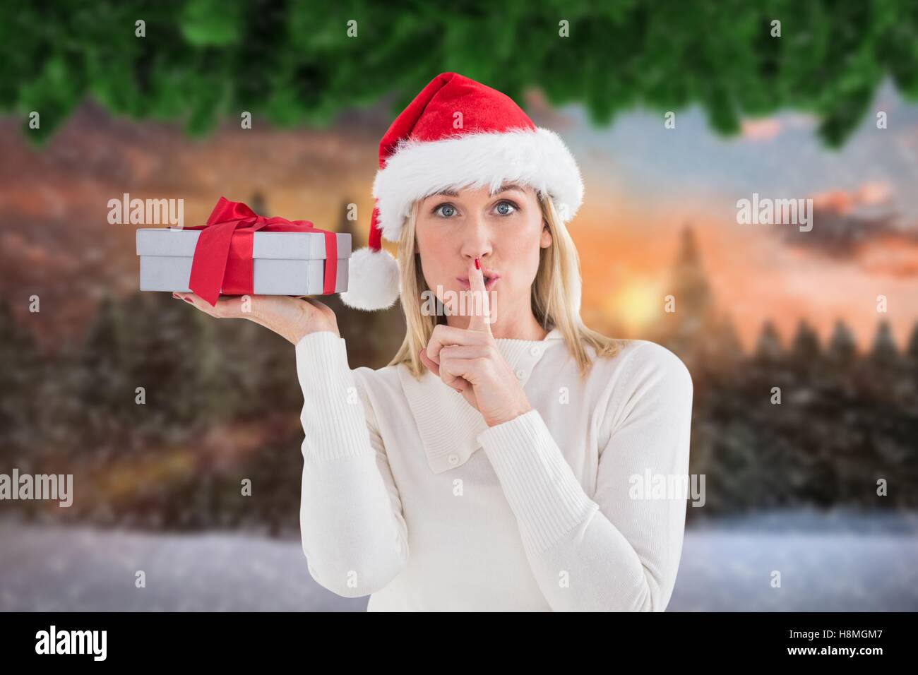 Beautiful woman in santa hat holding a gift box with finger on lips ...