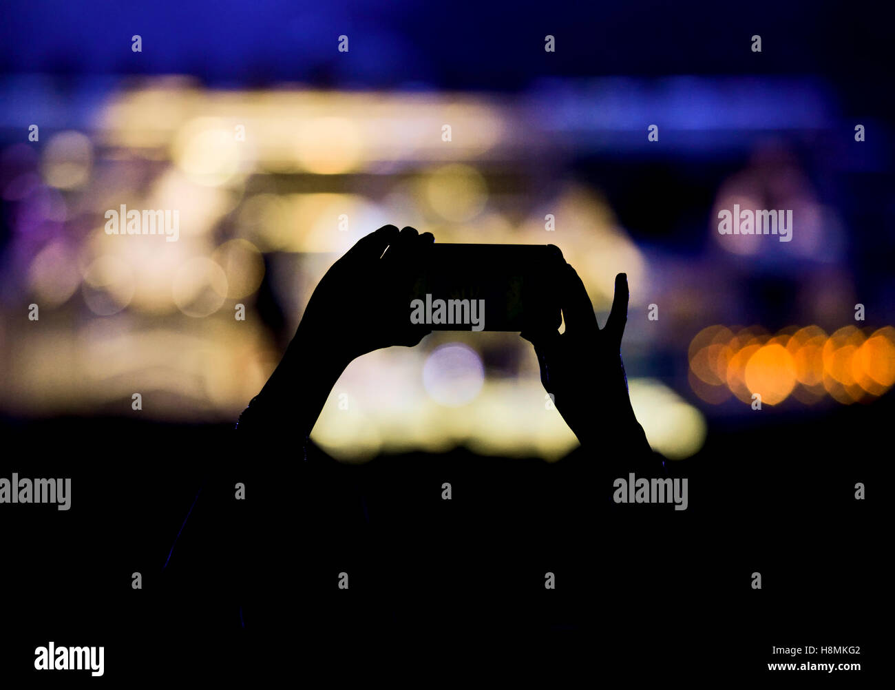 Concert stage with silhouetted hands raised holding camera phone Stock Photo