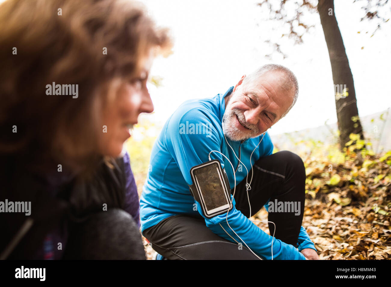 Senior runners in nature, tying shoelaces. Man with smartphone Stock