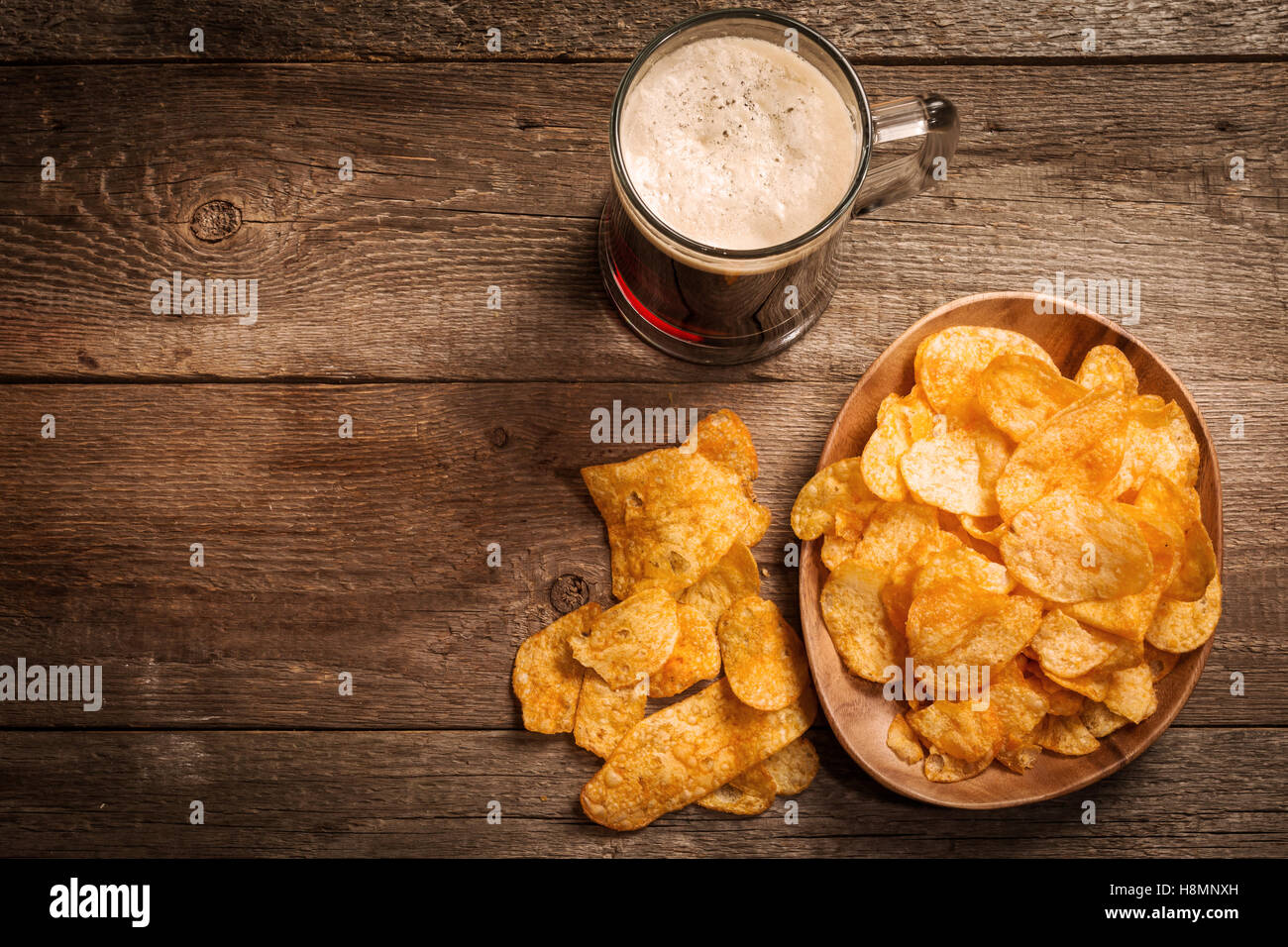 Glass of dark beer with potato chips on a wooden background. Top view ...