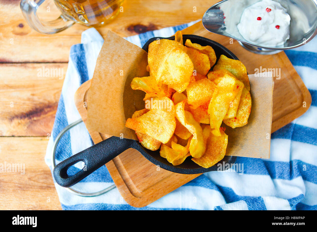 Potato chips in a frying pan with garlic sauce and beer on a wooden