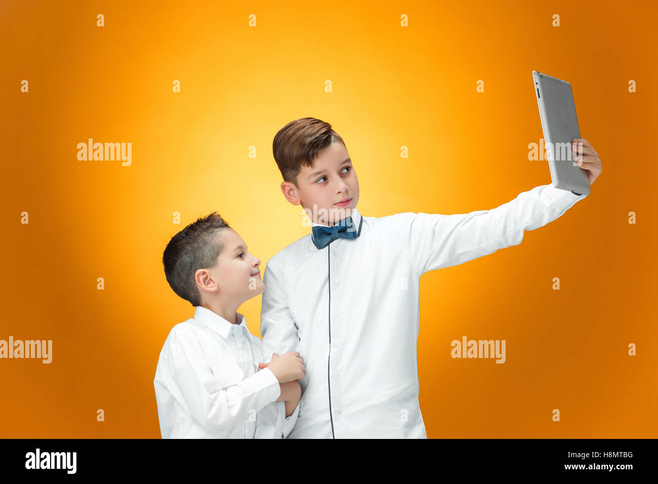 The two boys using laptop on orange background Stock Photo - Alamy