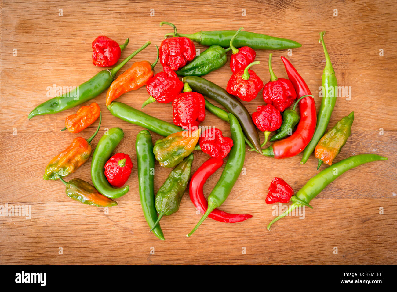Mixed hot chilli peppers on a wooden chopping block, Trinidad moruga scorpions, Norfolk nagas and long Joes Stock Photo