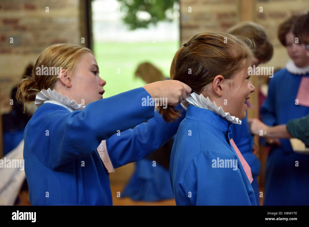 Choristers at cassock fitting and rehearsing for evensong. Girl chorister ties up hair of another girl chorister. Stock Photo