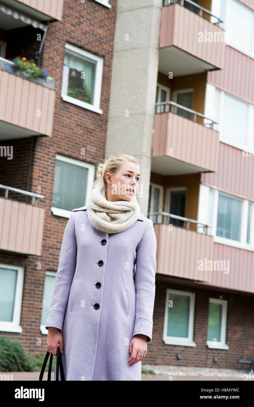 Young woman wearing overcoat standing against buildings Stock Photo