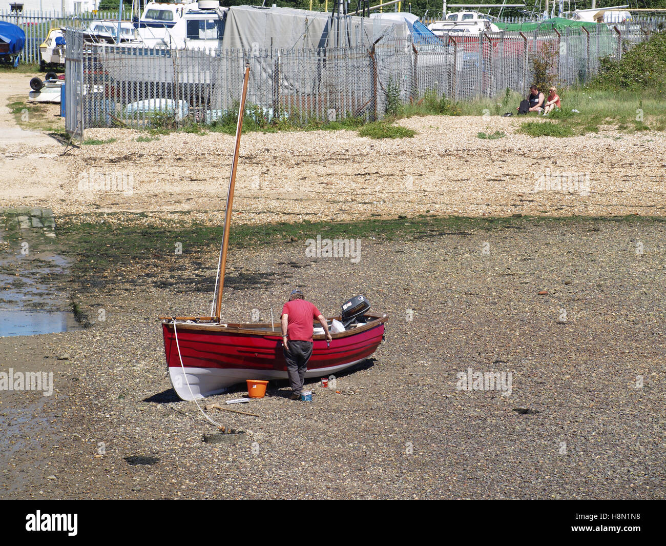 Man working on maintaining red fishing boat at Weston Shore, Woolston, Southampton, Hampshire UK Stock Photo
