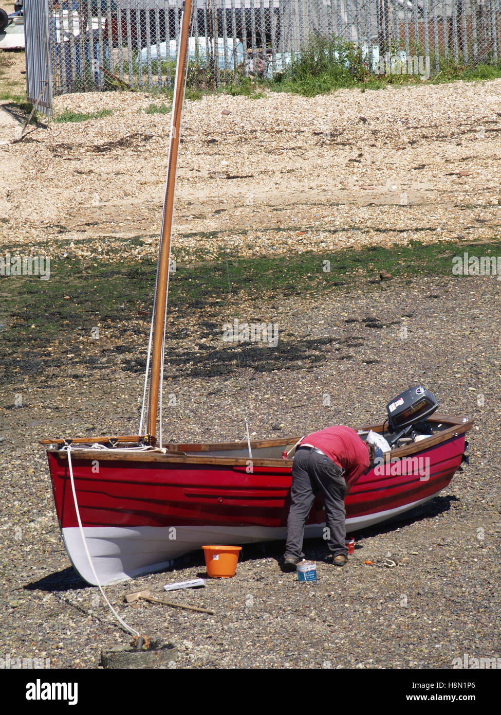 Man working on maintaining red fishing boat at Weston Shore, Woolston, Southampton, Hampshire UK Stock Photo