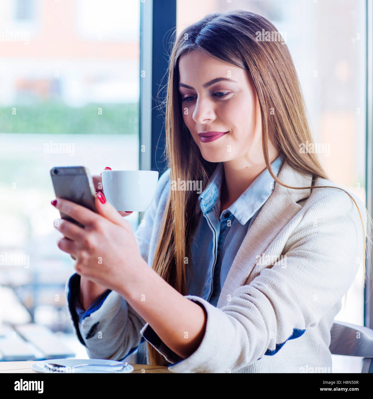 Beautiful Young Woman Drinking Coffee and Looking at her phone Stock Photo