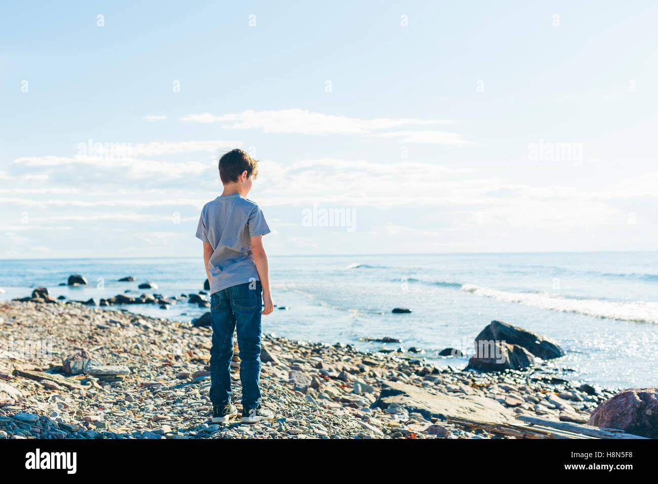 Boy (8-9) standing on rocky beach Stock Photo