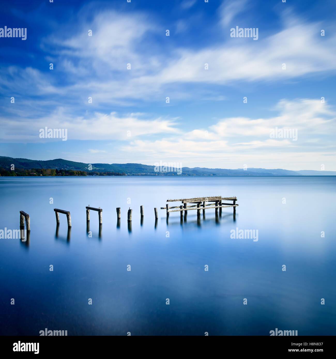 Wooden pier or jetty remains on a blue lake sunset. Long Exposure photography Stock Photo