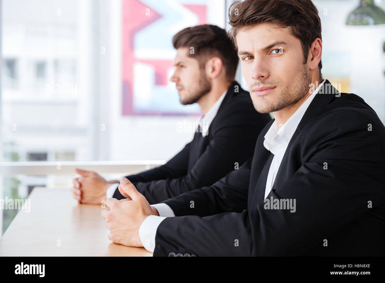 Two serious young businessmen in suit sitting in office Stock Photo - Alamy