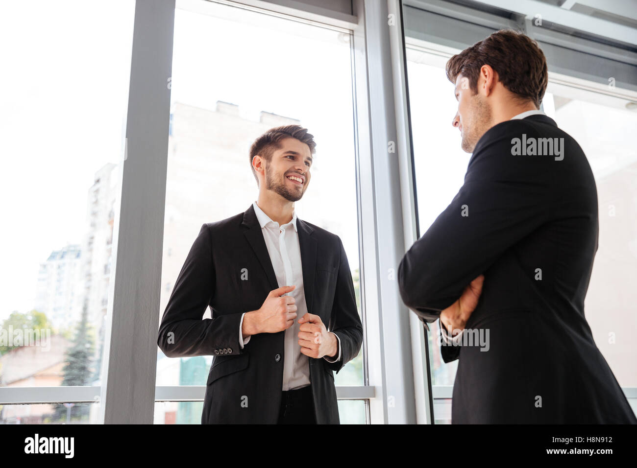 Two cheerful young businessmen talking in office near the window Stock ...