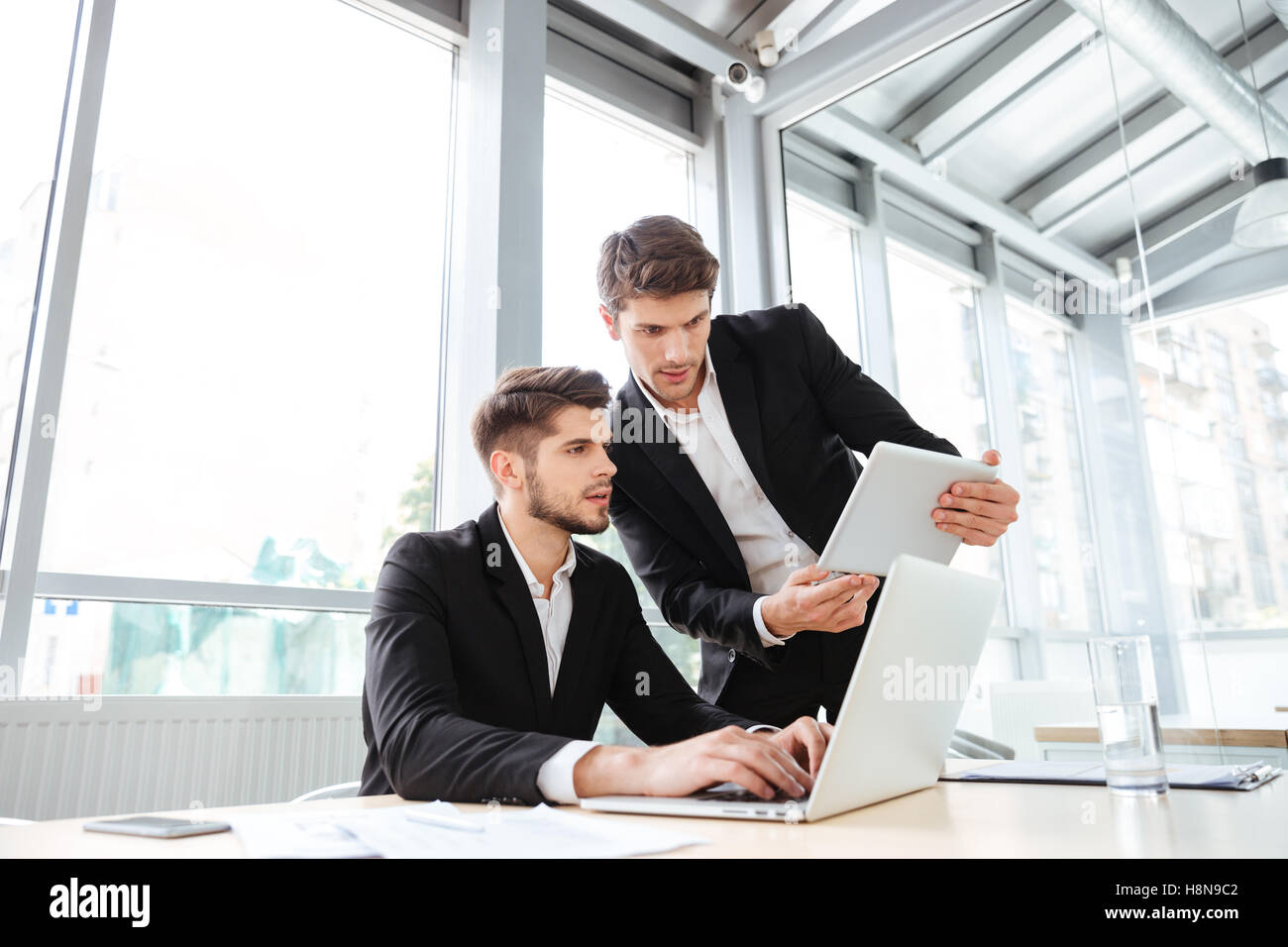 Two serious young businessmen using laptop and tablet in office together Stock Photo