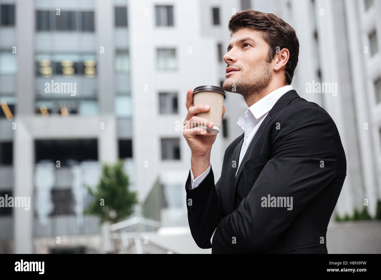 Thoughtful young businessman drinking take away coffee and thinking near business center Stock Photo