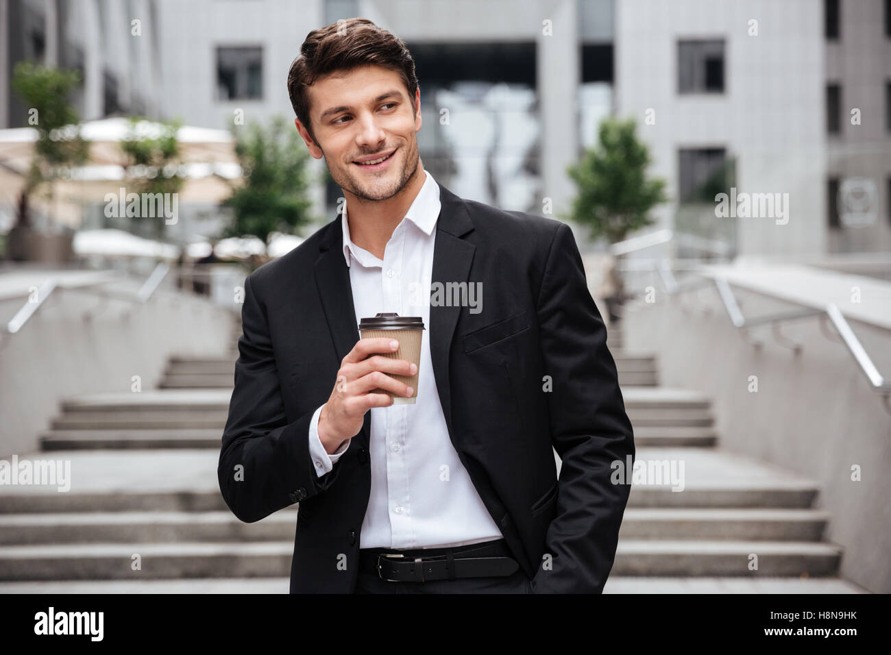 Happy attractive young businessman smiling and drinking coffee in the city Stock Photo