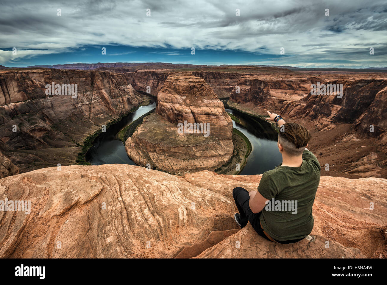 Horseshoe Bend, Colorado river and a hiker sitting at the edge and enjoying the panoramic view. Stock Photo