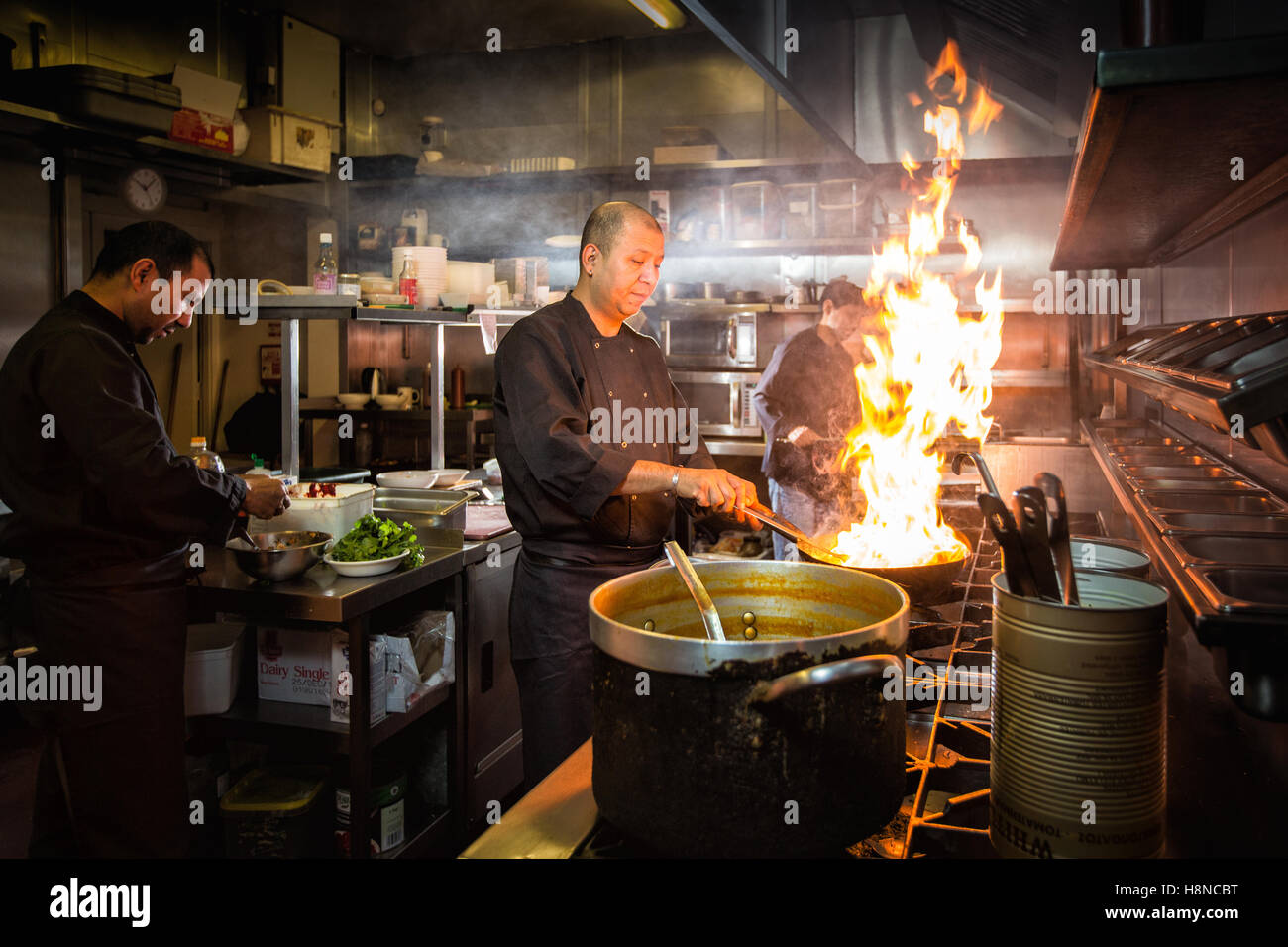 Nepalese chefs cooking in a restaurant kitchen with pans and flames ...