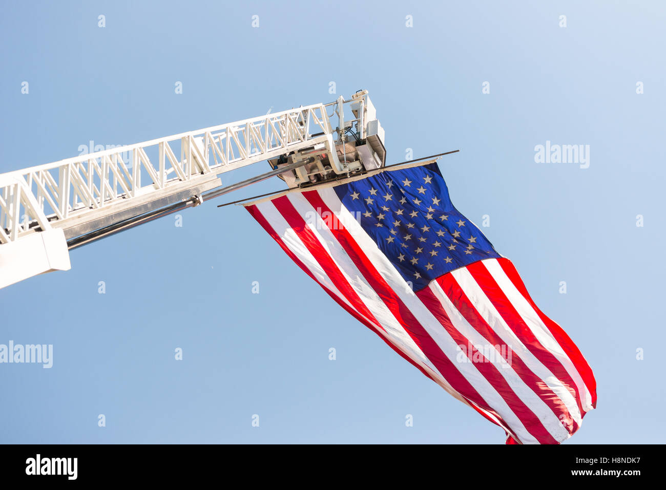 The flag of The United States of America is displayed hanging from extended ladder of a fire department rescue ladder platform. Stock Photo