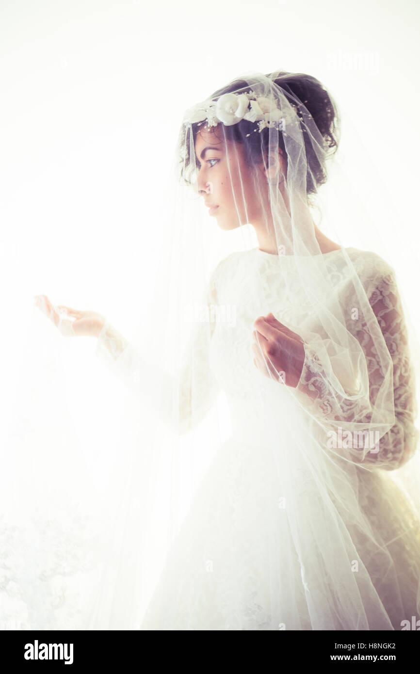 Bridal wedding photography: A young olive skinned woman wearing a white wedding dress and a veil  standing in front of a white background, UK Stock Photo