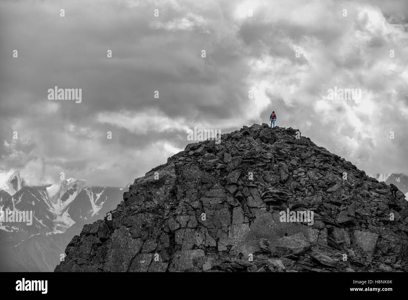 Silhouette of a girl with backpack on huge mountain. Very far. Epic black-and-white photo. Stock Photo