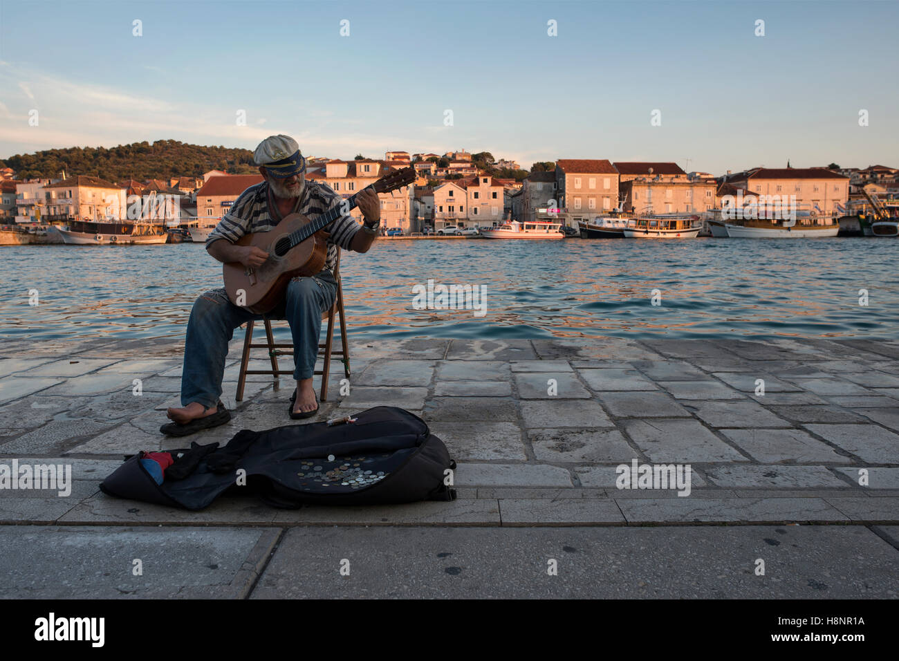 An old sailor playing guitar in the port of Trogir with view of the ...