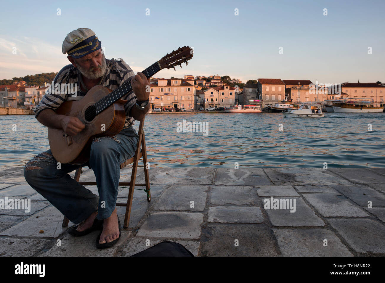 An old sailor playing guitar in the port of Trogir with view of the ...