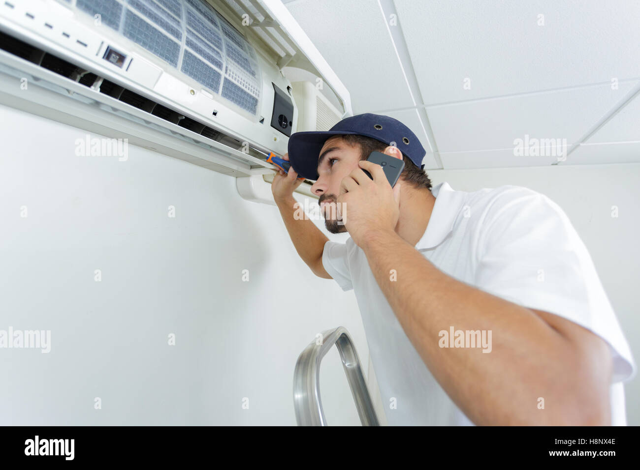 young handyman repairing air conditioning system calling for help Stock