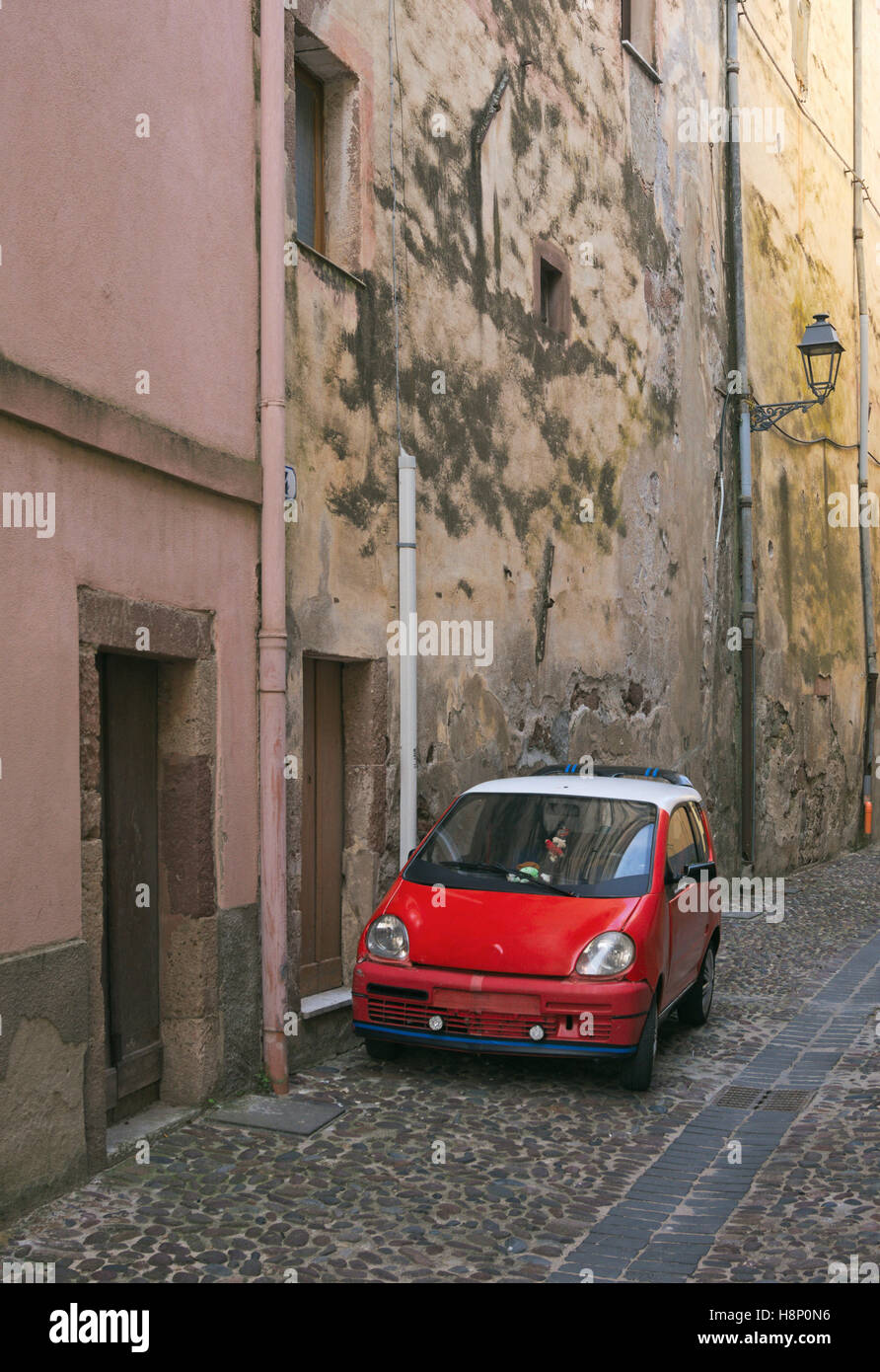 a red city car parked on a narrow street of Bosa, Sardinia, Italy Stock Photo