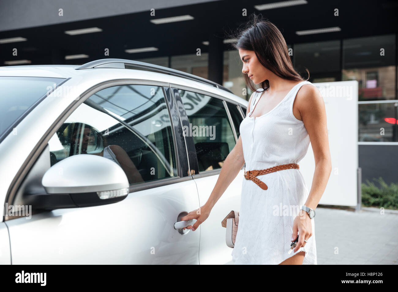 Beautiful young woman standing and opening the door in her car outdoors Stock Photo