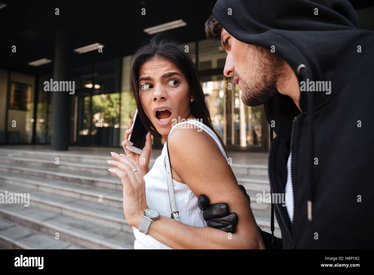 Frightened young woman with mobile phone shouting and being attacked by criminal man on the street Stock Photo