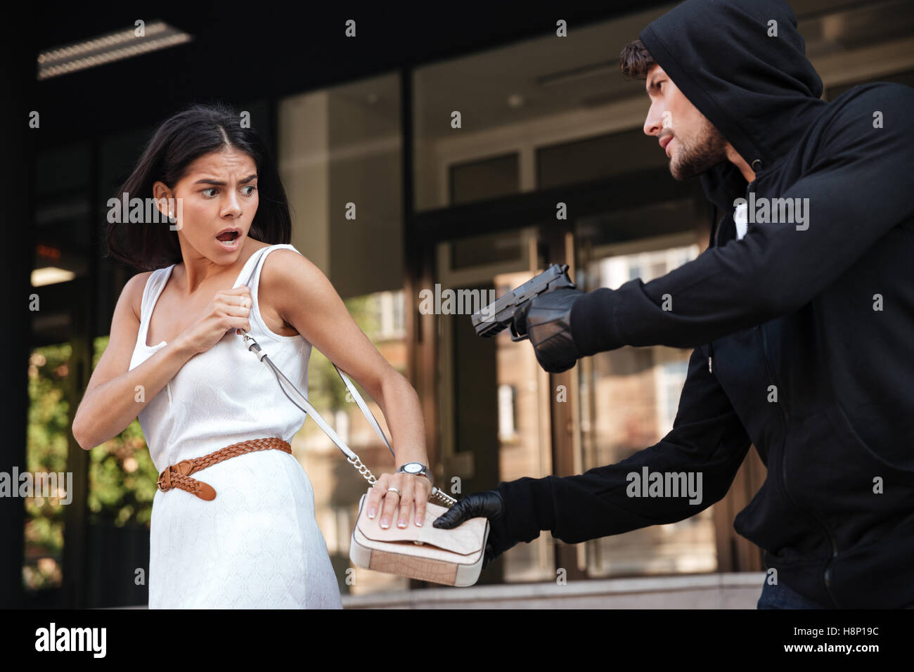 Criminal man with gun stealing bag of scared young woman on the street Stock Photo