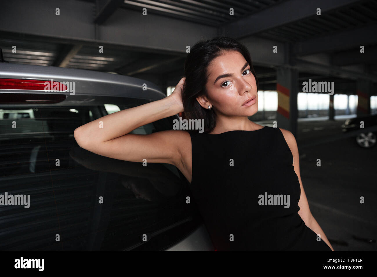 Portrait of beautiful young woman in black dress standing near her car on parking Stock Photo