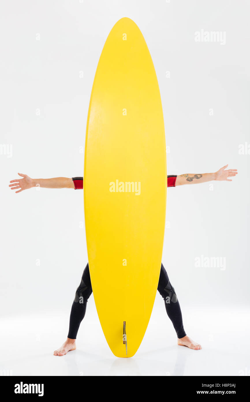 Funny surfer standing behind surfboard with outstretched arms isolated on the white background Stock Photo