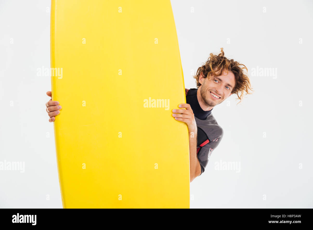 Cheerful smiling sportsman looking out of the surfboard isolated on the white background Stock Photo