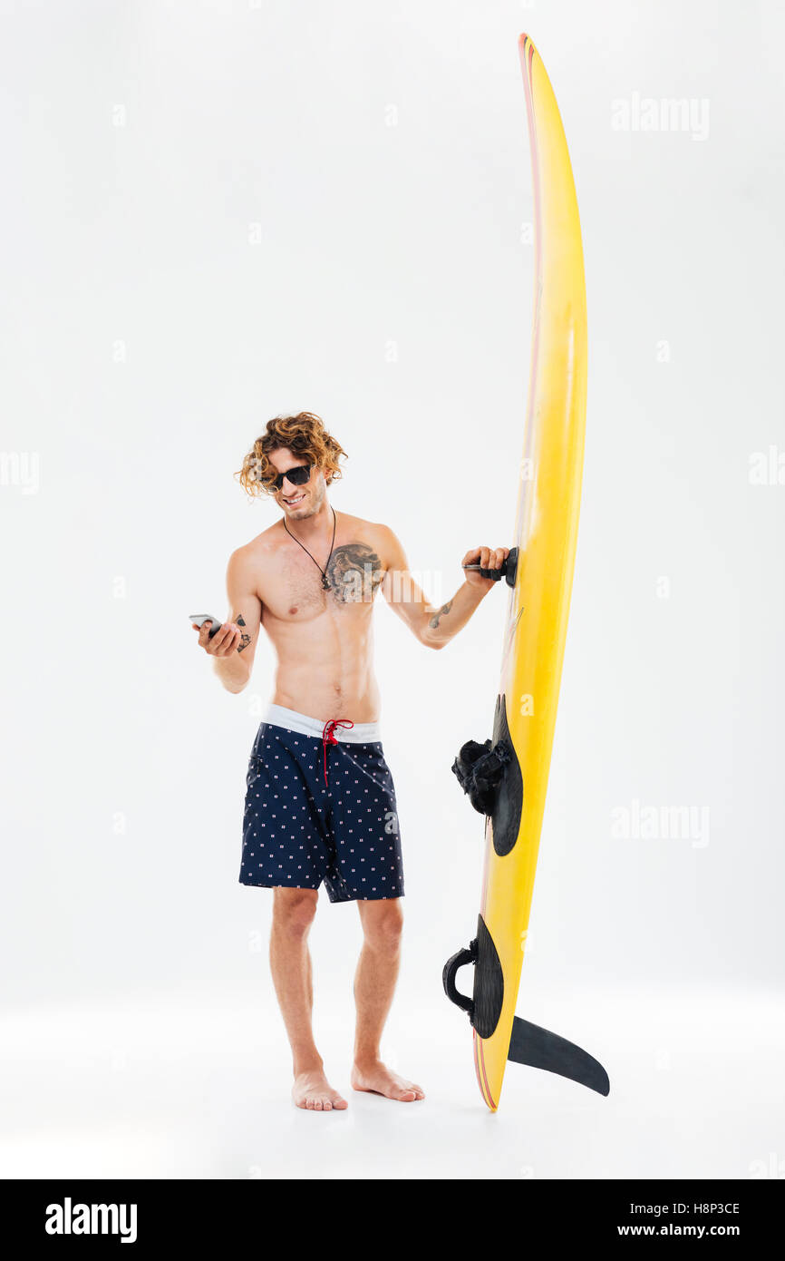 Happy young sportsman holding surfboard and using mobile phone isolated on the white background Stock Photo