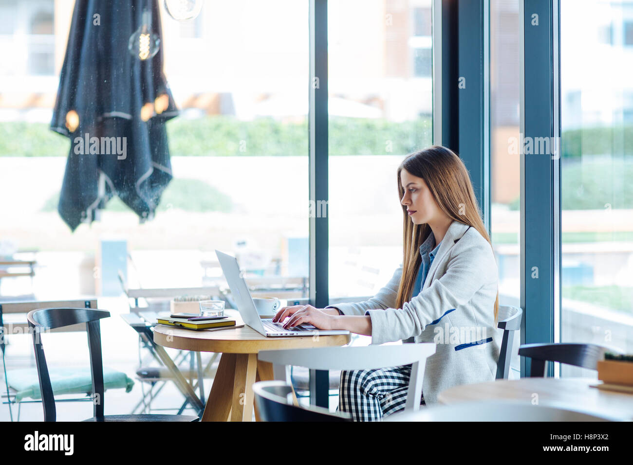Beautiful Young Woman Sitting in Coffee Shop and Working on Laptop Stock Photo