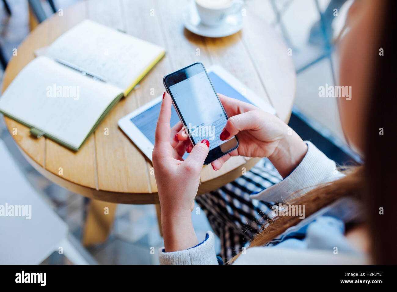 Young Woman Sitting in Coffee Shop and Typing on Phone Stock Photo
