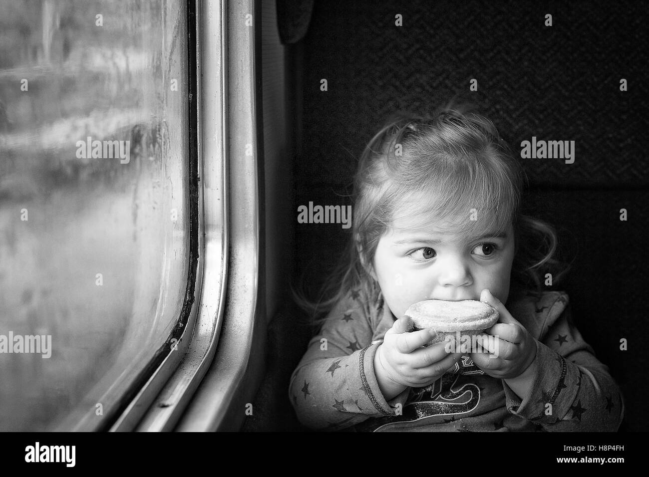 Cute innocent little girl traveling by train in England eating a mince pie at Christmas time Stock Photo