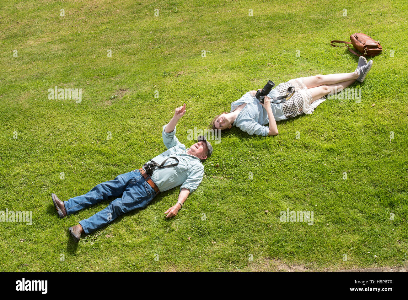 UK, England, Yorkshire, Richmond - An above view of a young female tourist and an old man with their cameras laying in a field l Stock Photo