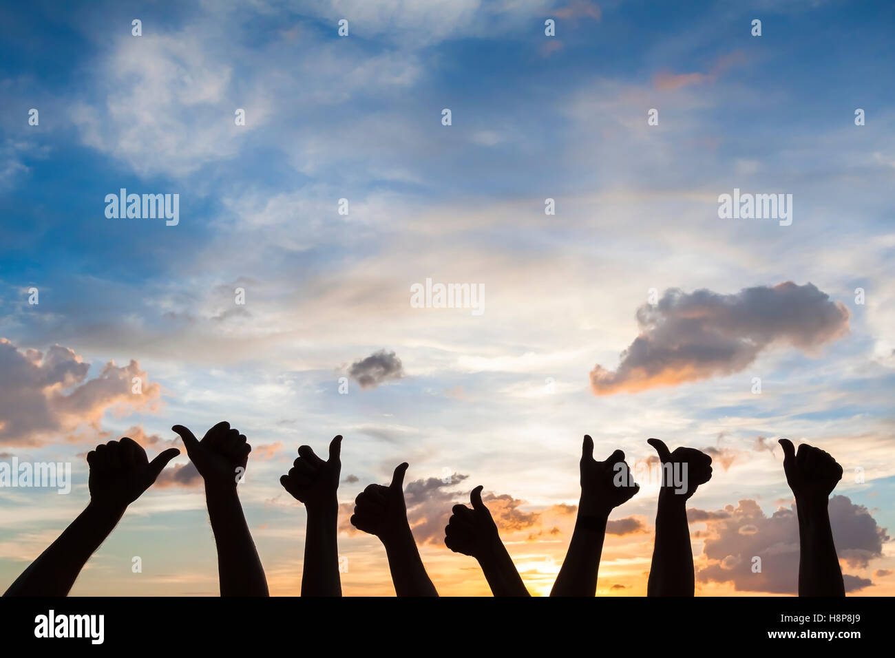 Silhouette of many people with thumbs up, symbol of like, satisfaction and agreement, sky background Stock Photo