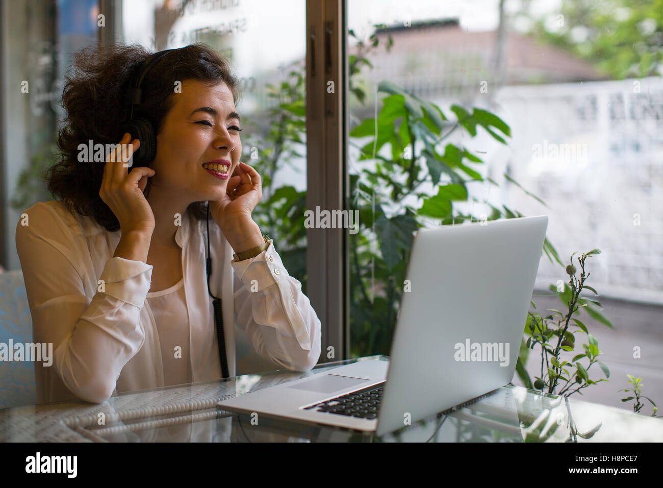 Asian girl enjoying music in headphones sitting with a laptop in a cafe. Stock Photo