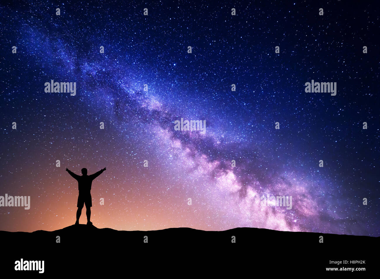 Purple Milky Way with silhouette of a standing man with raised up arms ...