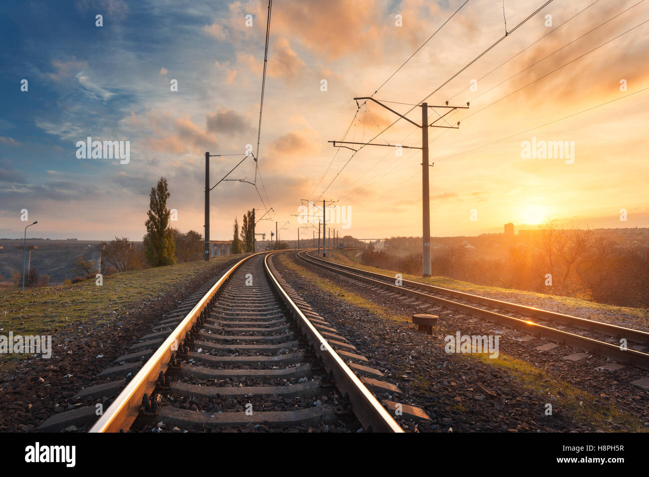 Railroad against beautiful sky at sunset. Industrial landscape with railway station, colorful blue sky with clouds, trees and gr Stock Photo