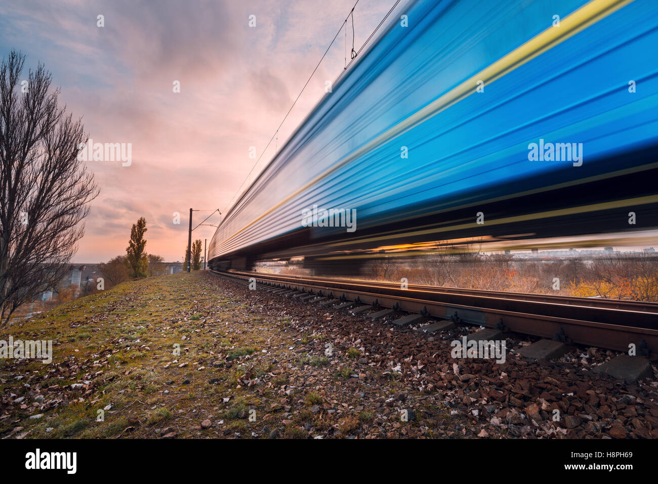 High speed blue passenger train on railroad track in motion at sunset. Blurred commuter train. Railway station with cloudy sky. Stock Photo