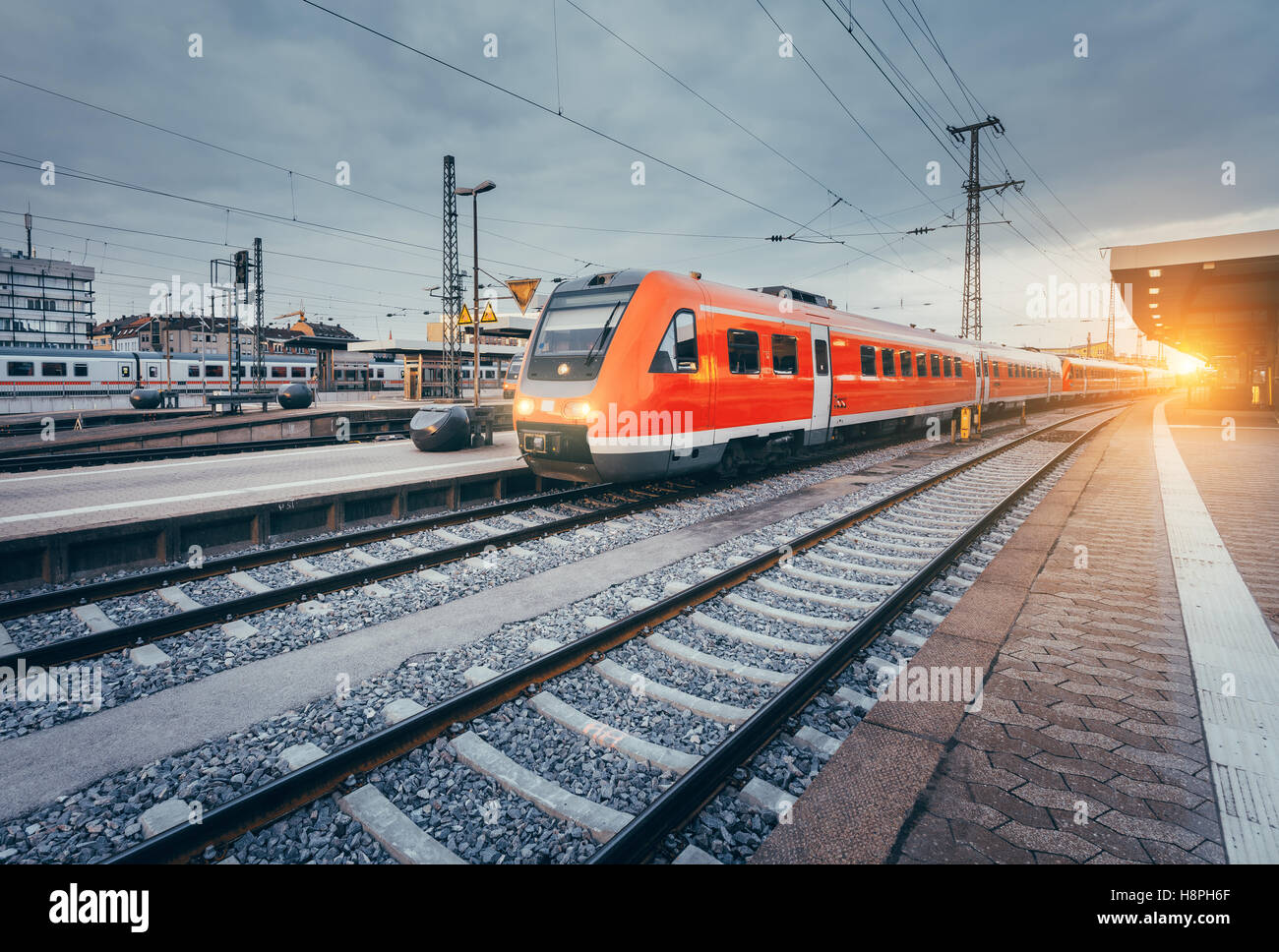 Modern high speed red commuter train at the railway station at colorful sunset. Railroad with vintage toning. Train at railway Stock Photo