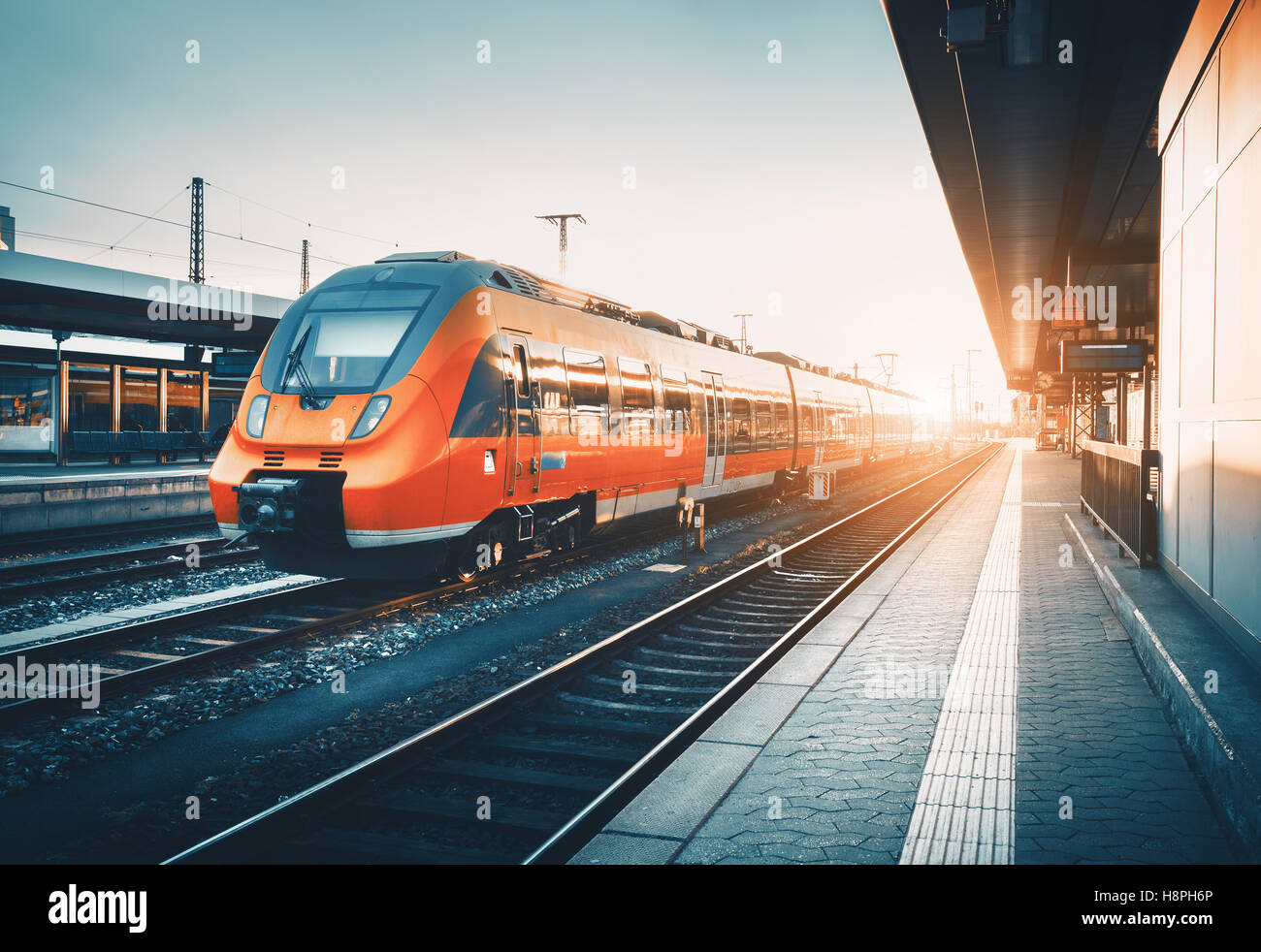 Modern high speed red commuter train at the railway station at colorful sunset. Railroad with vintage toning. Train at railway p Stock Photo